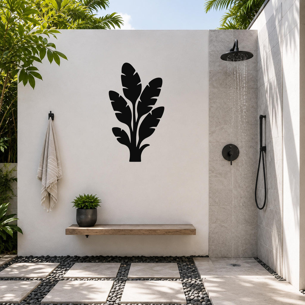 Black metal tropical leaves wall art silhouette mounted on a white outdoor wall above a wooden bench in a patio shower area.