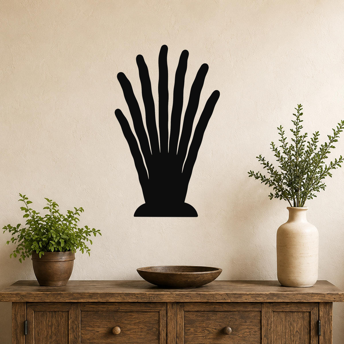 Black metal wall art in a silhouette of a hand with spread fingers, mounted on a beige wall above a wooden console table with plants.