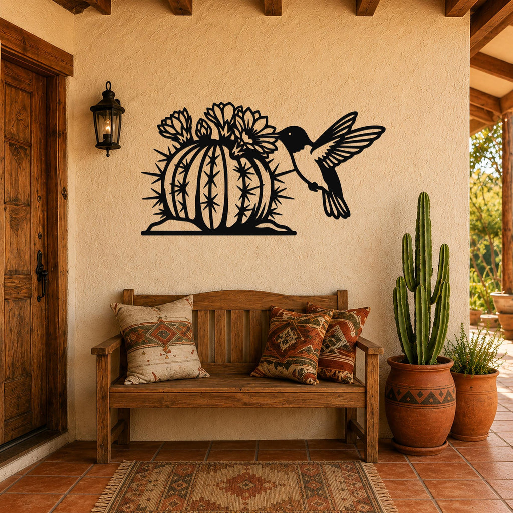 Black metal wall art featuring a hummingbird and flowering barrel cactus cutout, mounted on a stucco wall above a wooden bench in a southwestern-style entryway.