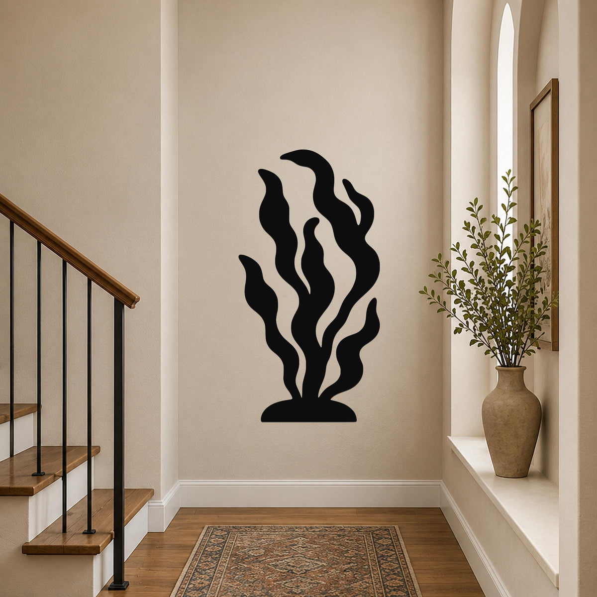 Black metal kelp wall art with flowing leaf cutouts, mounted on a hallway wall above a patterned rug near a staircase.