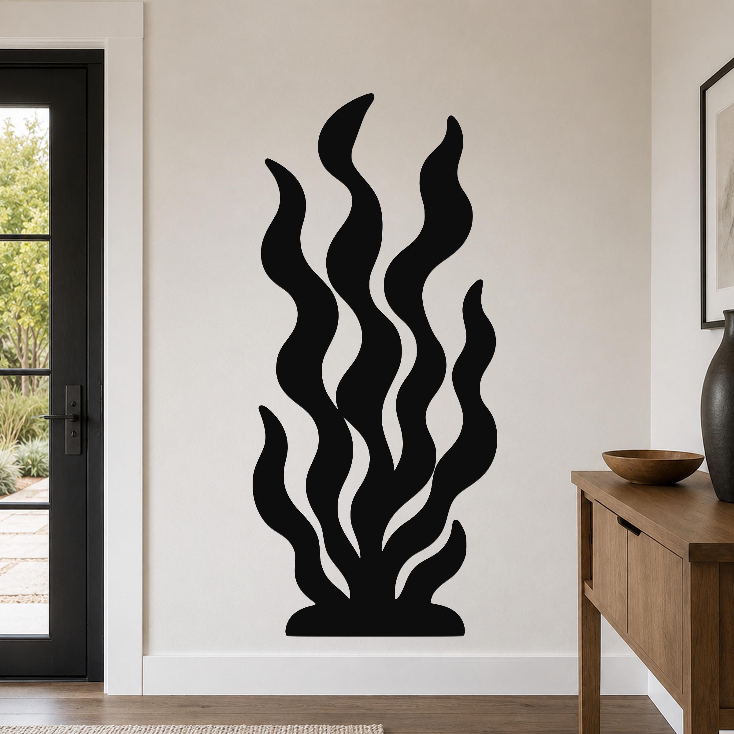 Black metal wall art in a kelp or seaweed silhouette design, mounted on a light-colored wall above a wooden console table in a modern entryway.