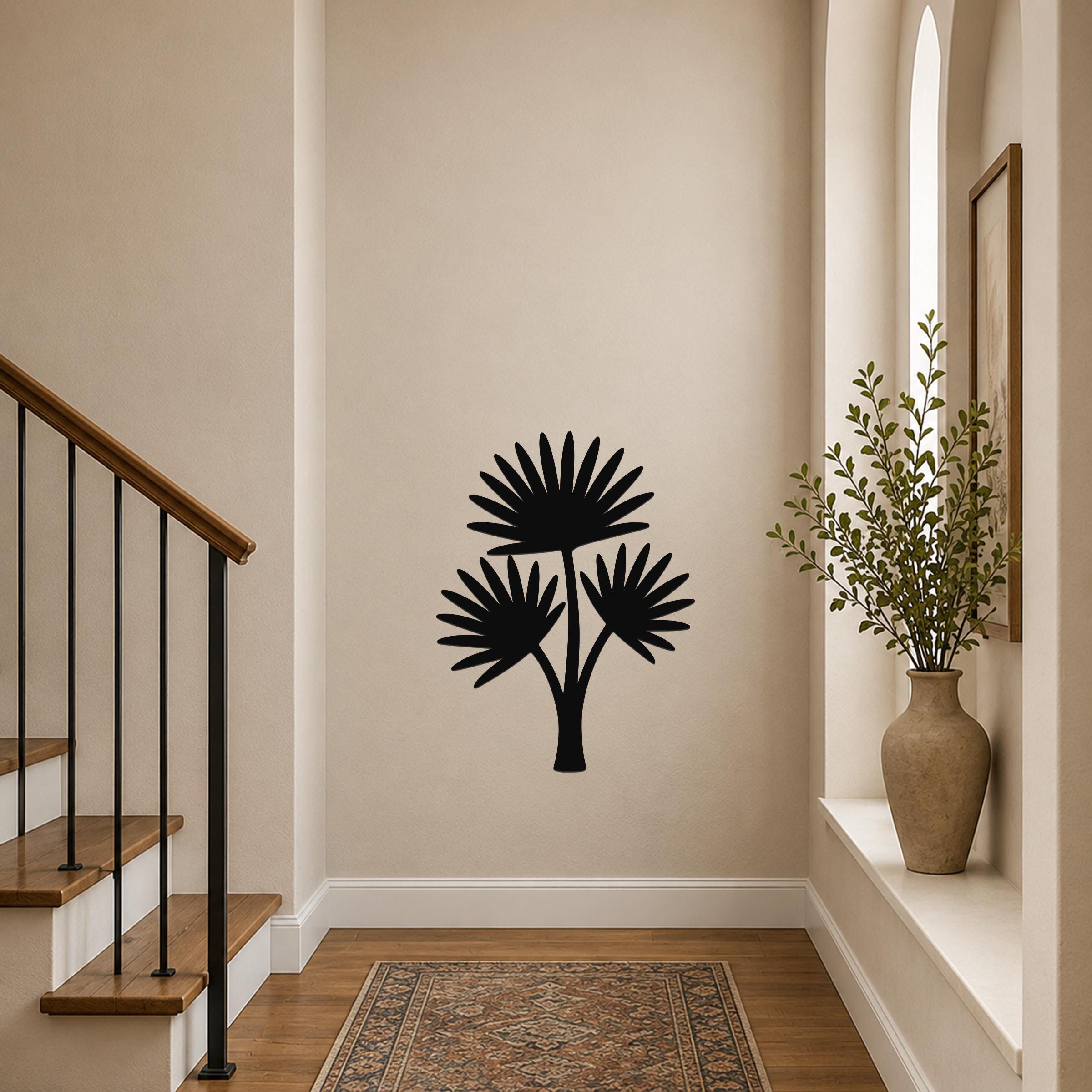 Black metal cutout wall art of a fan palm tree with three fronds, mounted on a beige hallway wall above a patterned rug near a staircase.