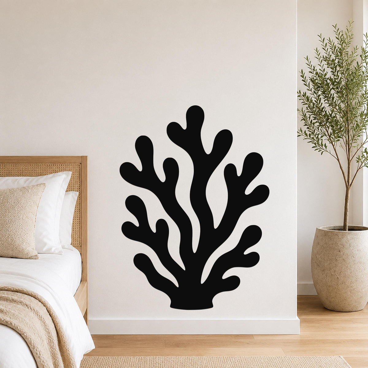 Black metal coral wall art with branching cutouts, mounted on a white bedroom wall above a bed.