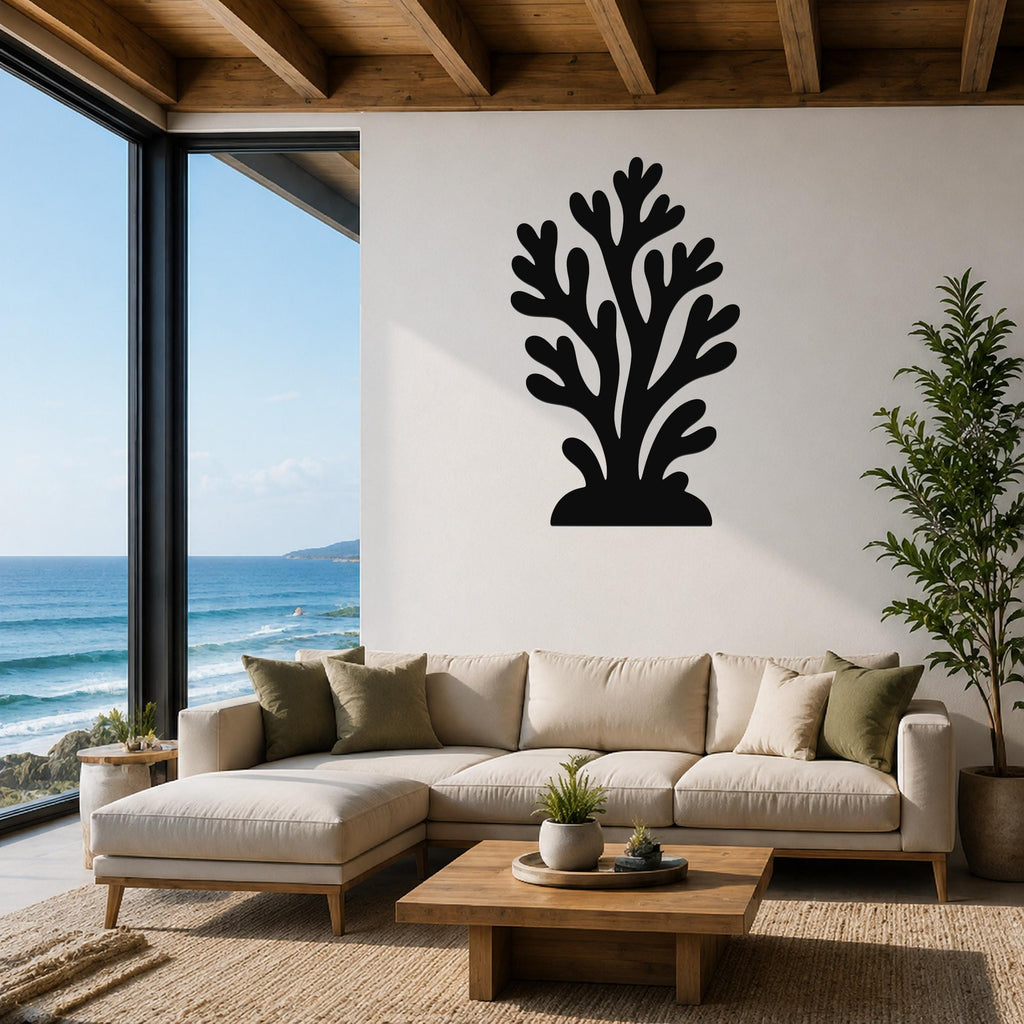 Black metal coral wall art with branching cutouts, mounted on a white wall above a beige sectional sofa in a living room with ocean views.