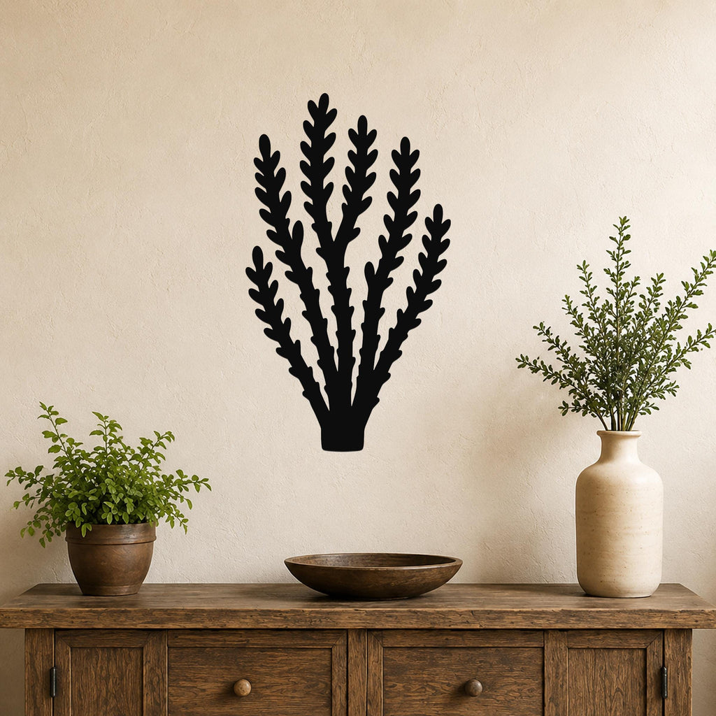Black metal wall art in a branching cactus silhouette, mounted on a beige wall above a wooden console table with potted plants.