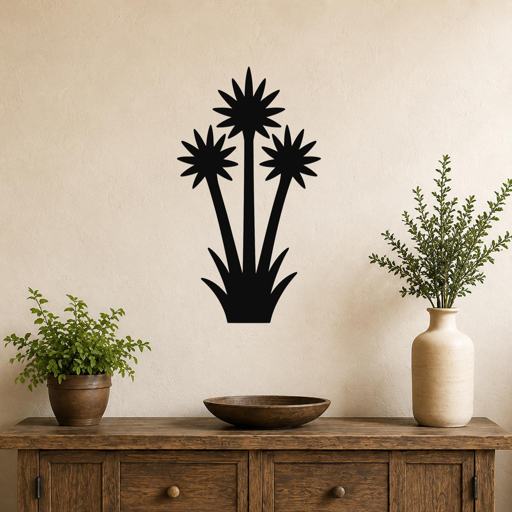 Black metal wall art cutout of a blooming yucca plant with three star-shaped flowers and spiky leaves, mounted on a beige wall above a wooden console table.