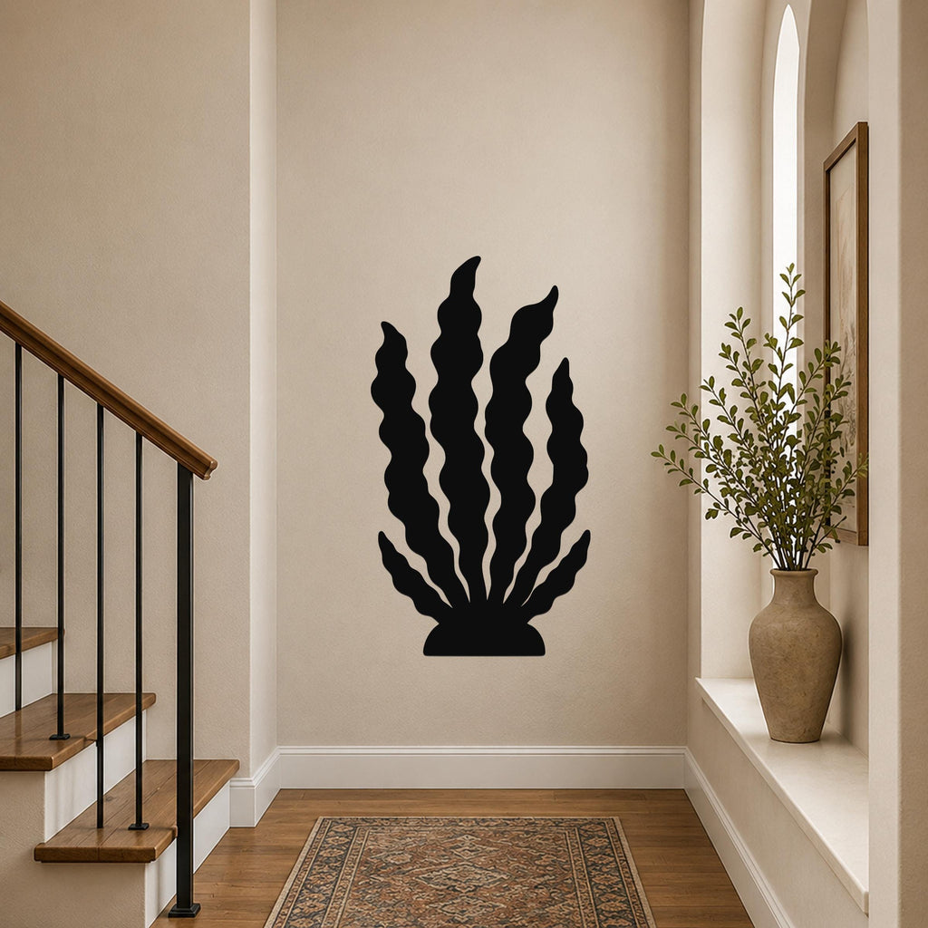 Black metal wall art in a kelp or seaweed silhouette, mounted on a hallway wall above a patterned rug near a staircase.