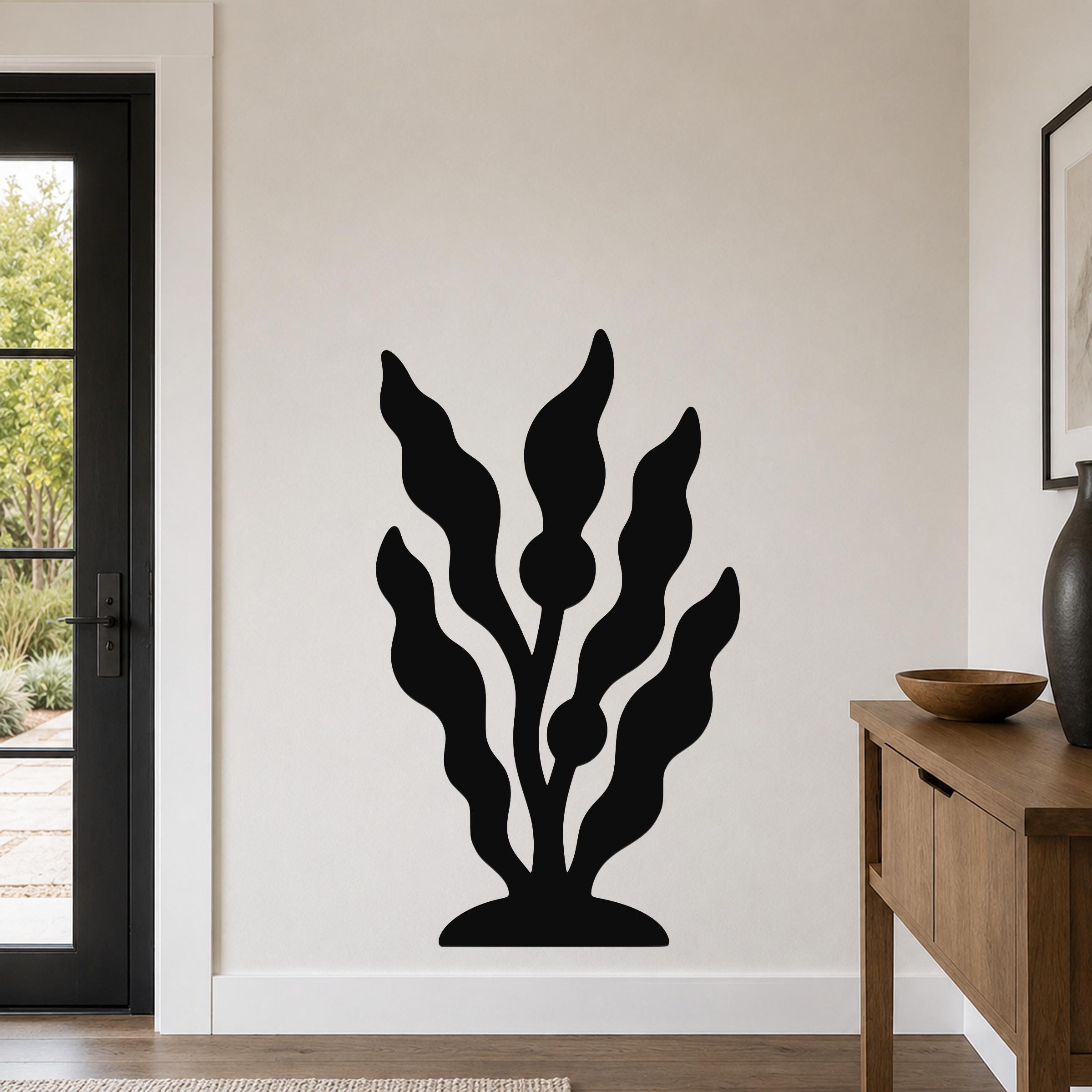Black metal wall art in a kelp or seaweed silhouette design, mounted on a light-colored wall in a living room near a door and console table.