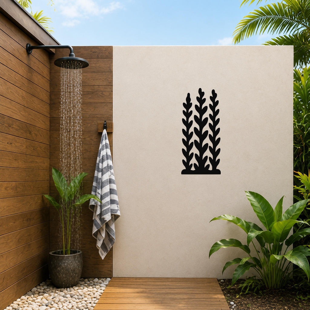 Black metal wall art with a kelp and seaweed silhouette design, mounted on a beige outdoor wall beside a wooden shower area.