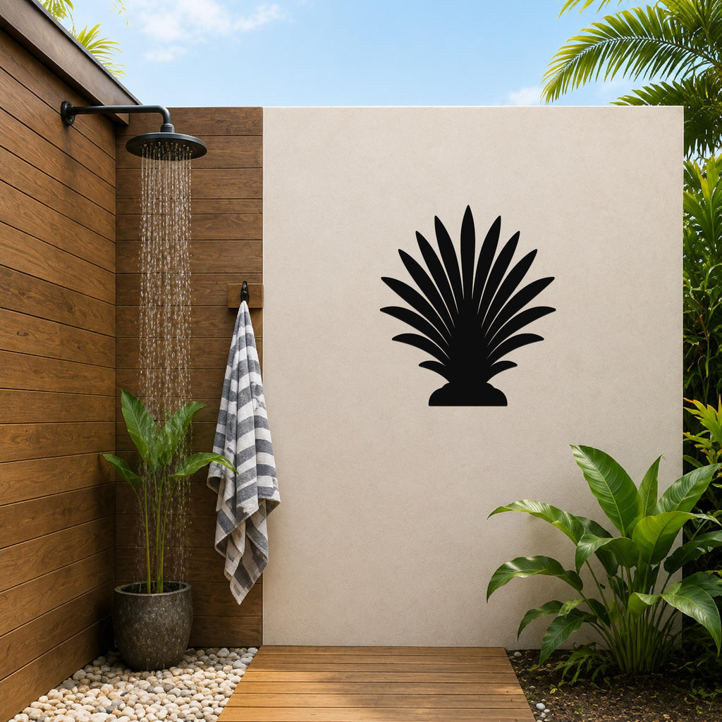 Black metal palm tree wall art silhouette mounted on a beige outdoor wall beside a wooden shower area with a running showerhead and potted plants.