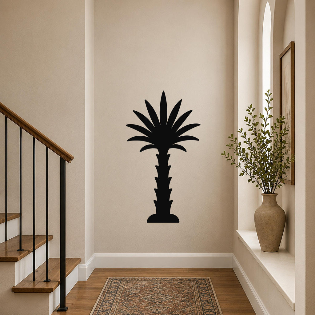 Black metal palm tree wall art silhouette mounted on a hallway wall above a patterned rug, with a staircase and vase of greenery visible nearby.
