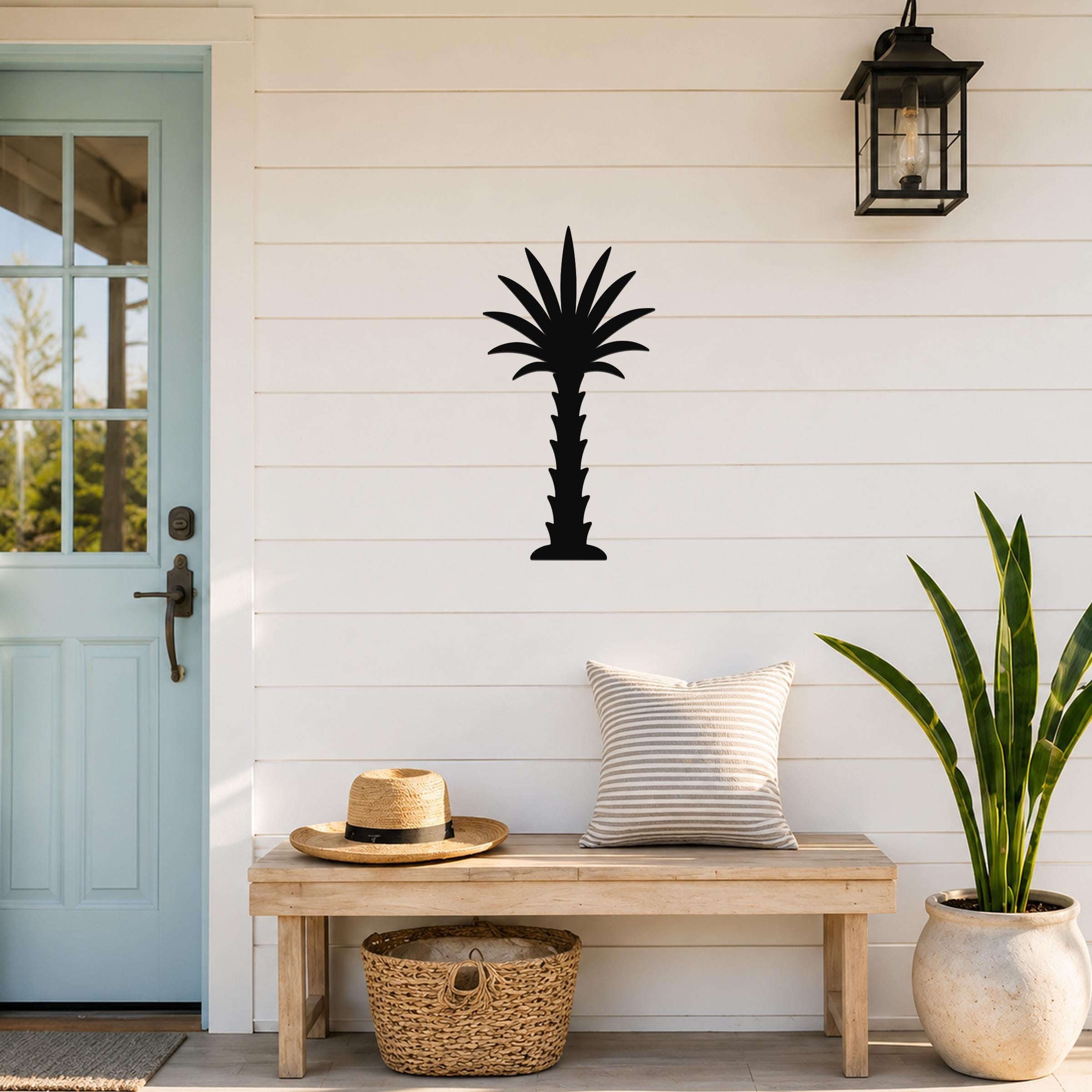 Black metal palm tree wall art silhouette mounted on a white shiplap wall above a wooden bench in a porch entryway.