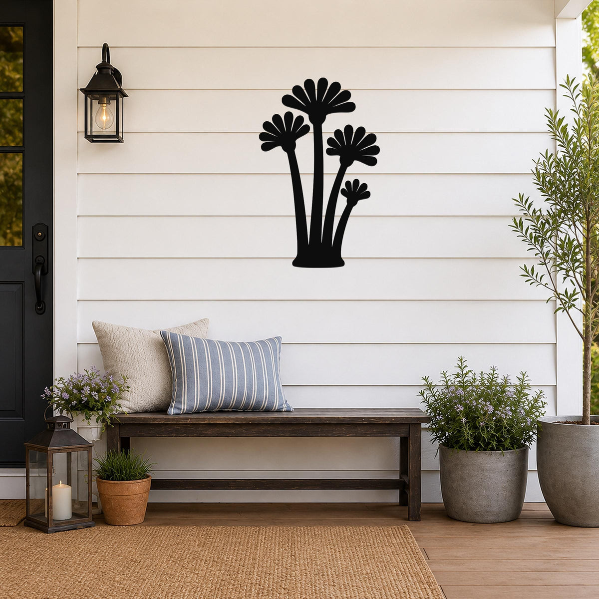 Black metal wall art featuring a silhouette of three fan palm trees, mounted on a white shiplap wall above a wooden bench on a porch.