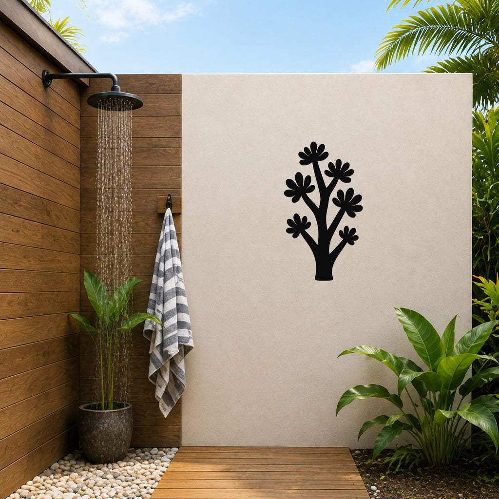Black metal wall art in a tree silhouette with flower cutouts, mounted on a beige outdoor wall beside a wooden shower area.