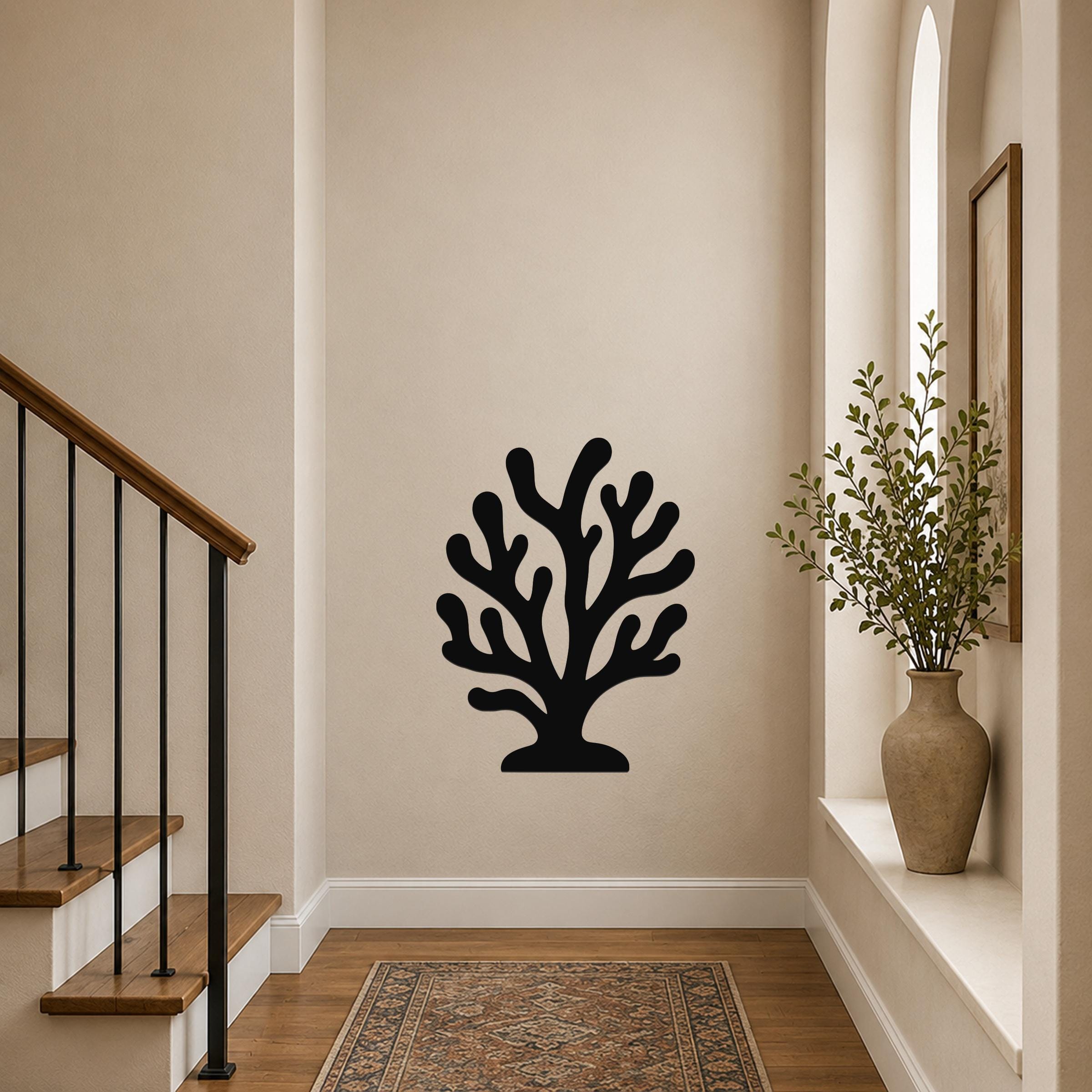 Black metal coral wall art with branching cutouts, mounted on a beige hallway wall near a staircase and window.