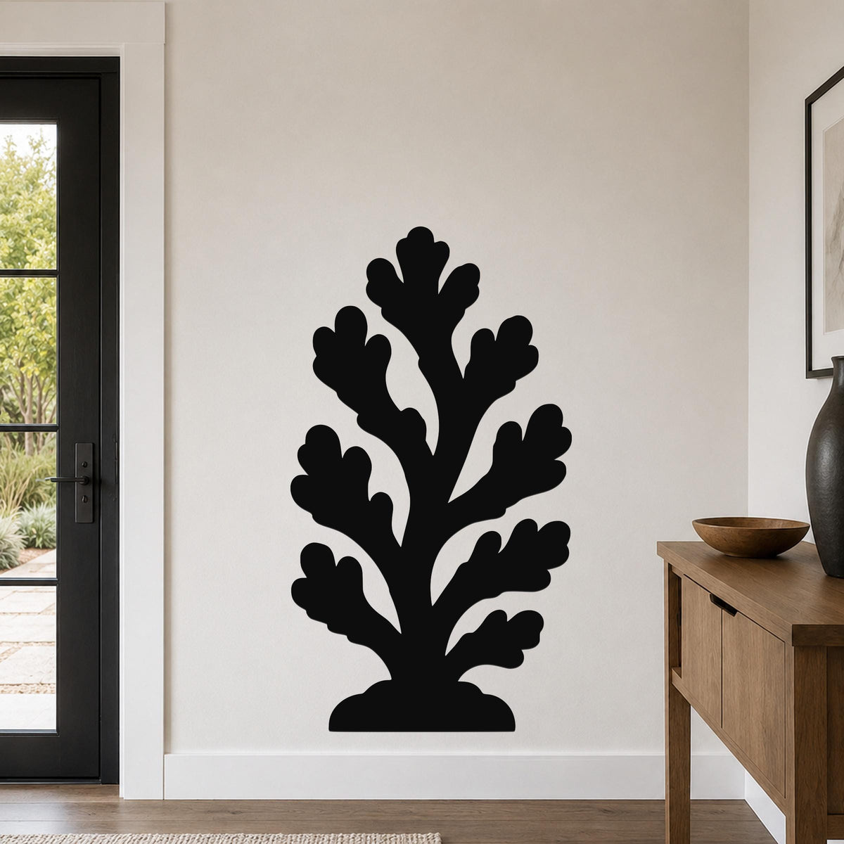 Black metal coral wall art with branching cutouts, mounted on a light-colored wall in a modern entryway.
