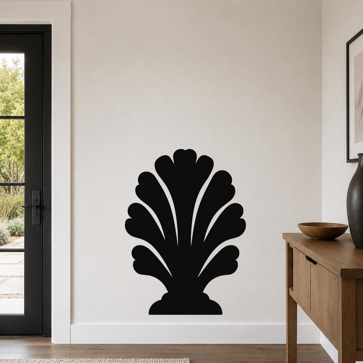 Black metal wall art in a coral or shell silhouette design, mounted on a light-colored wall above a wooden console table in a modern entryway.