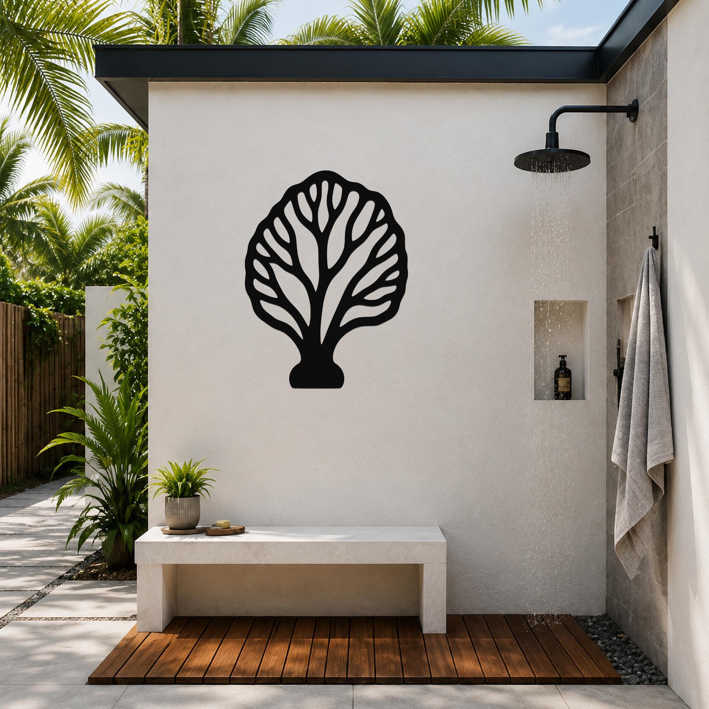 Black metal fan coral wall art with intricate branch cutouts, mounted on a white outdoor shower wall above a stone bench.