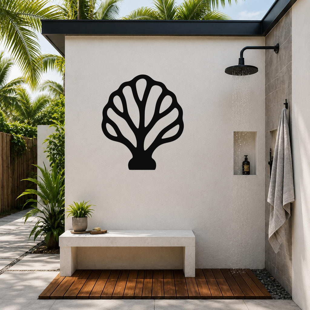 Black metal fan coral wall art with intricate cutout details, mounted on a white outdoor shower wall above a concrete bench in a tropical patio setting.