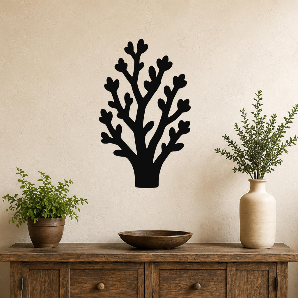 Black metal wall art in a tree silhouette with heart-shaped leaf cutouts, mounted on a beige wall above a wooden console table with potted plants.