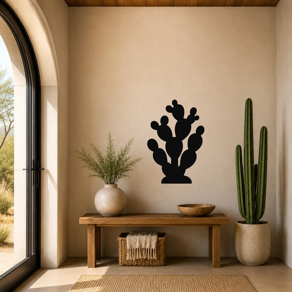 Black metal prickly pear cactus wall art with multiple rounded pads and cutout details, mounted on a beige wall above a wooden bench in a sunlit entryway.