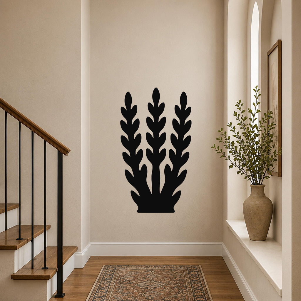 Black metal wall art with a kelp or seaweed silhouette design, mounted on a hallway wall above a patterned rug near a staircase.