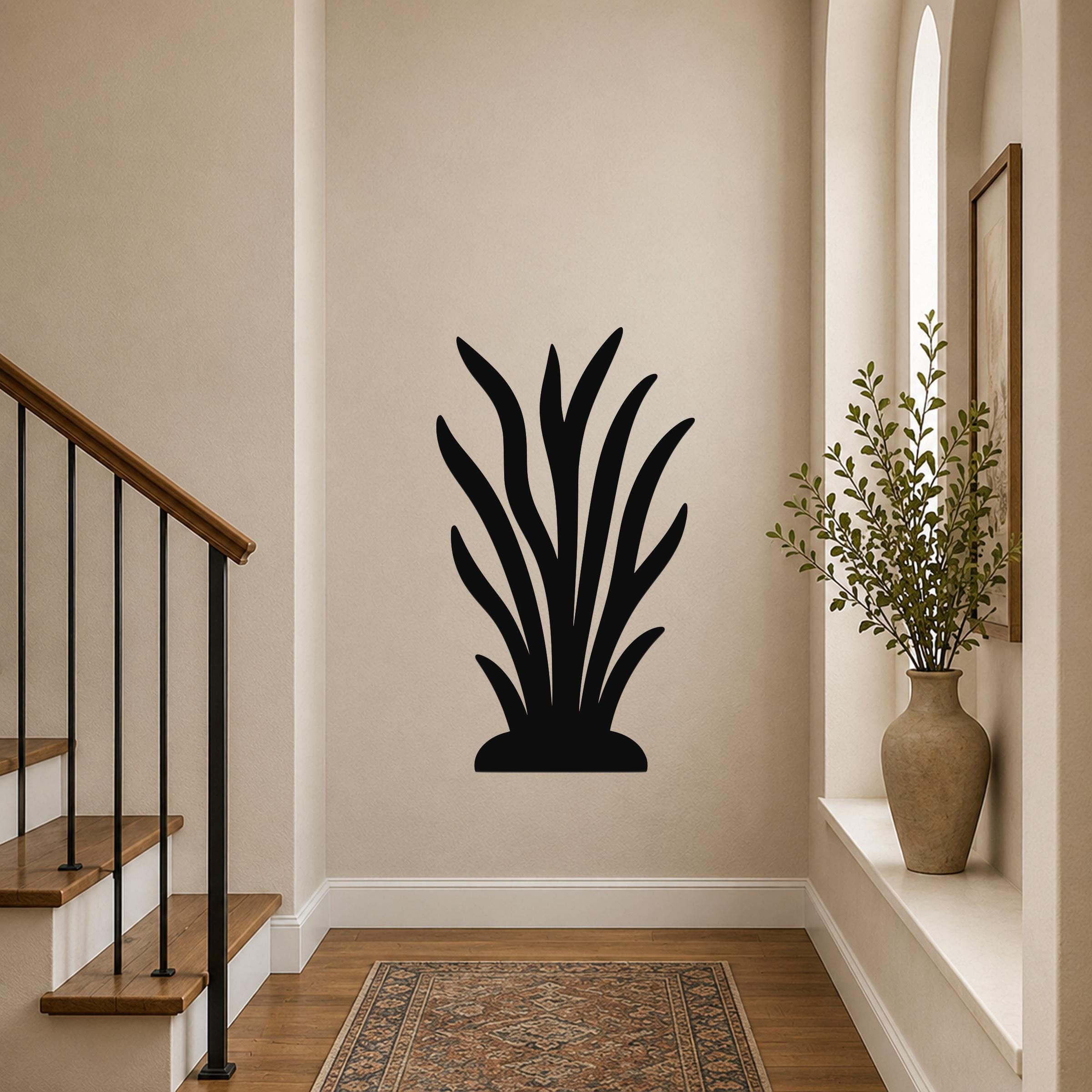 Black metal kelp wall art with leafy cutouts, mounted on a hallway wall above a patterned rug near a staircase.