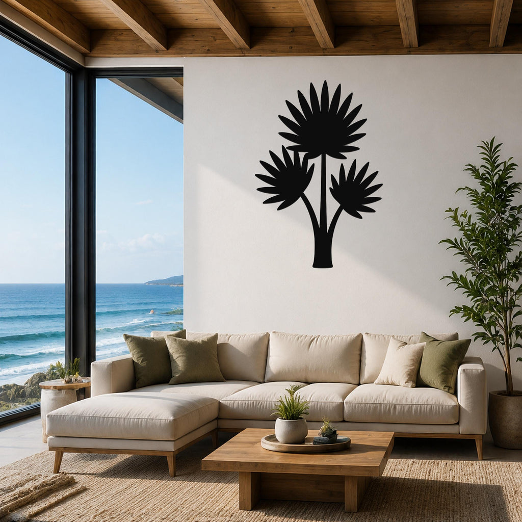 Black metal wall art of a fan palm tree silhouette, mounted on a white wall above a beige sectional sofa in a living room with ocean views.