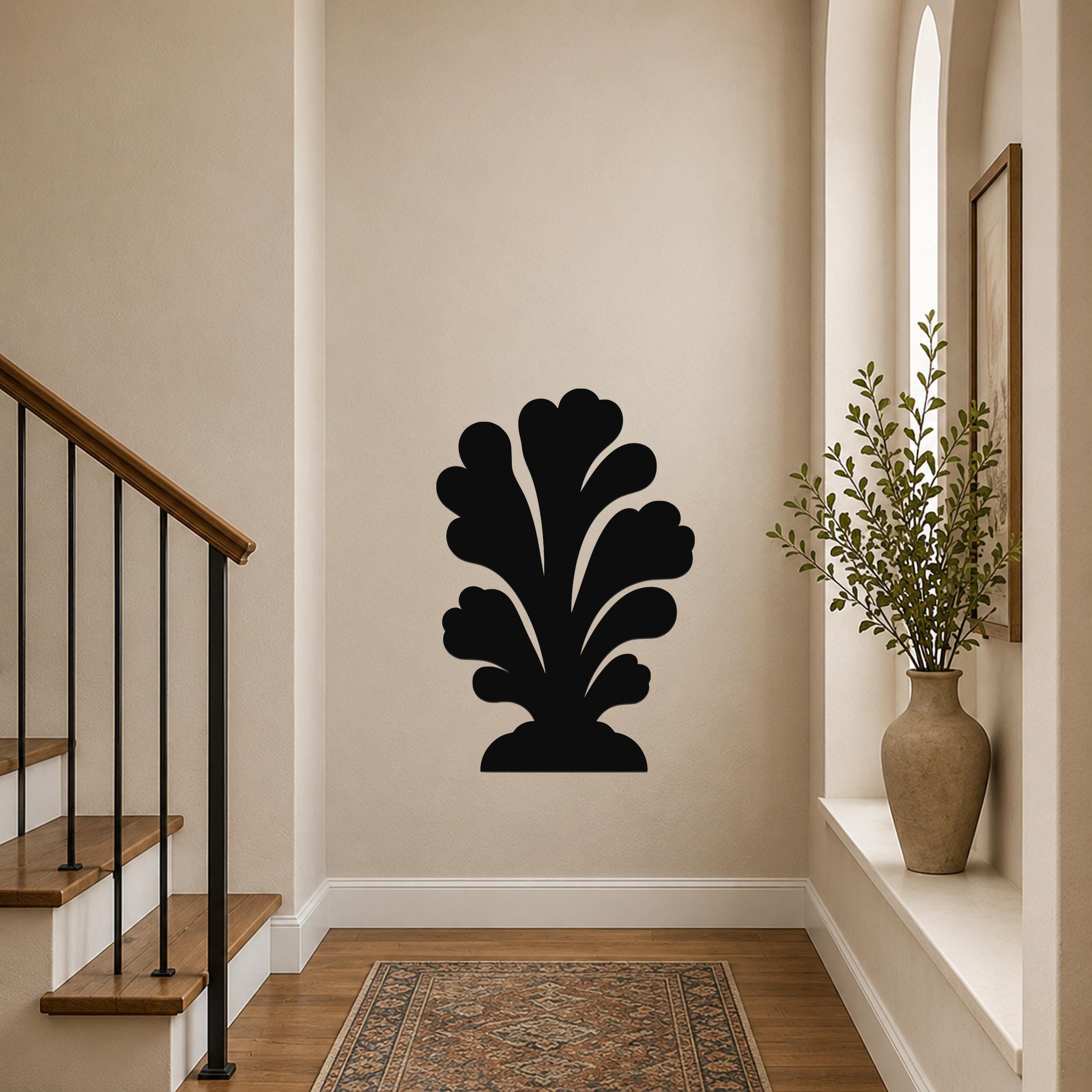 Black metal wall art in a leafy silhouette design, mounted on a hallway wall above a patterned rug near a staircase.