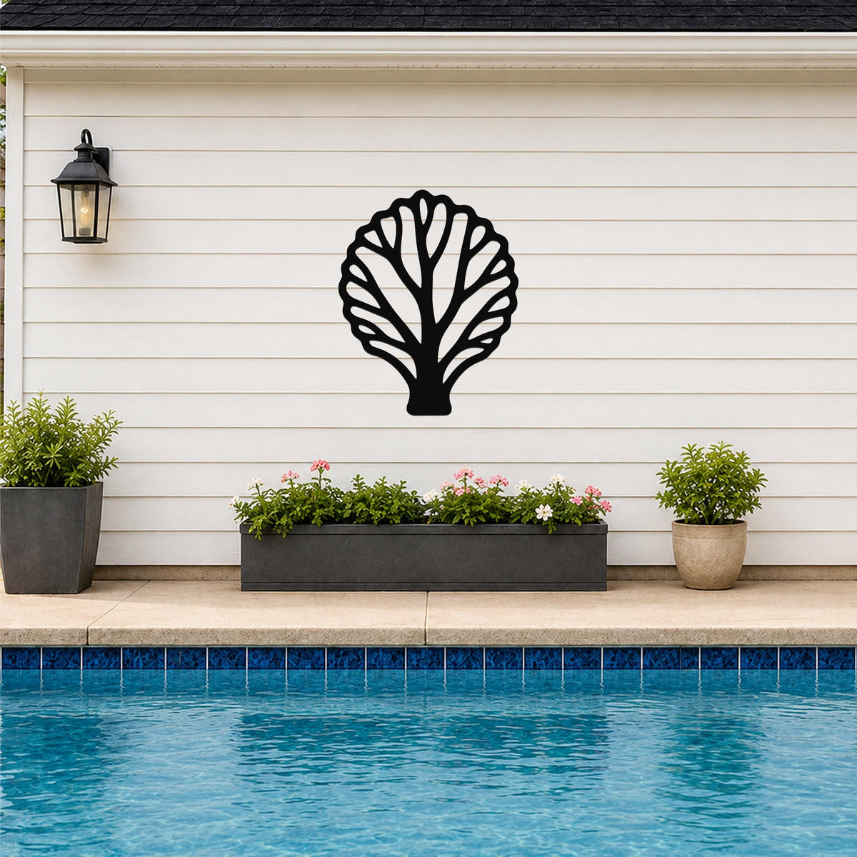 Black metal fan coral wall art with intricate branch cutouts, mounted on a white siding wall above a poolside planter.