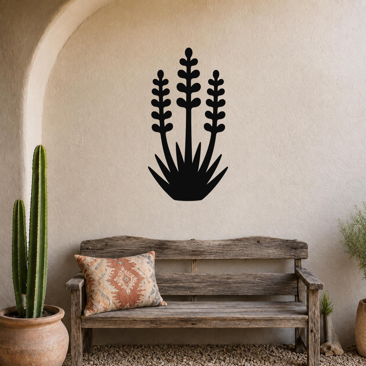 Black metal wall art in a yucca plant silhouette with three tall stems and spiky leaves, mounted on a textured beige wall above a wooden bench in a desert-style patio.