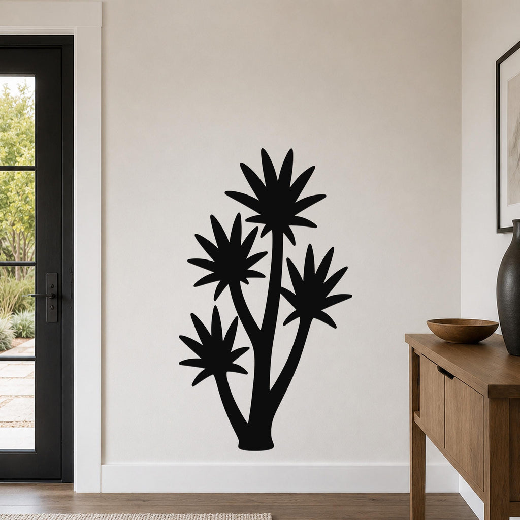 Black metal wall art featuring a tall yucca plant silhouette with four starburst-shaped leaves, mounted on a light-colored wall in a modern entryway.