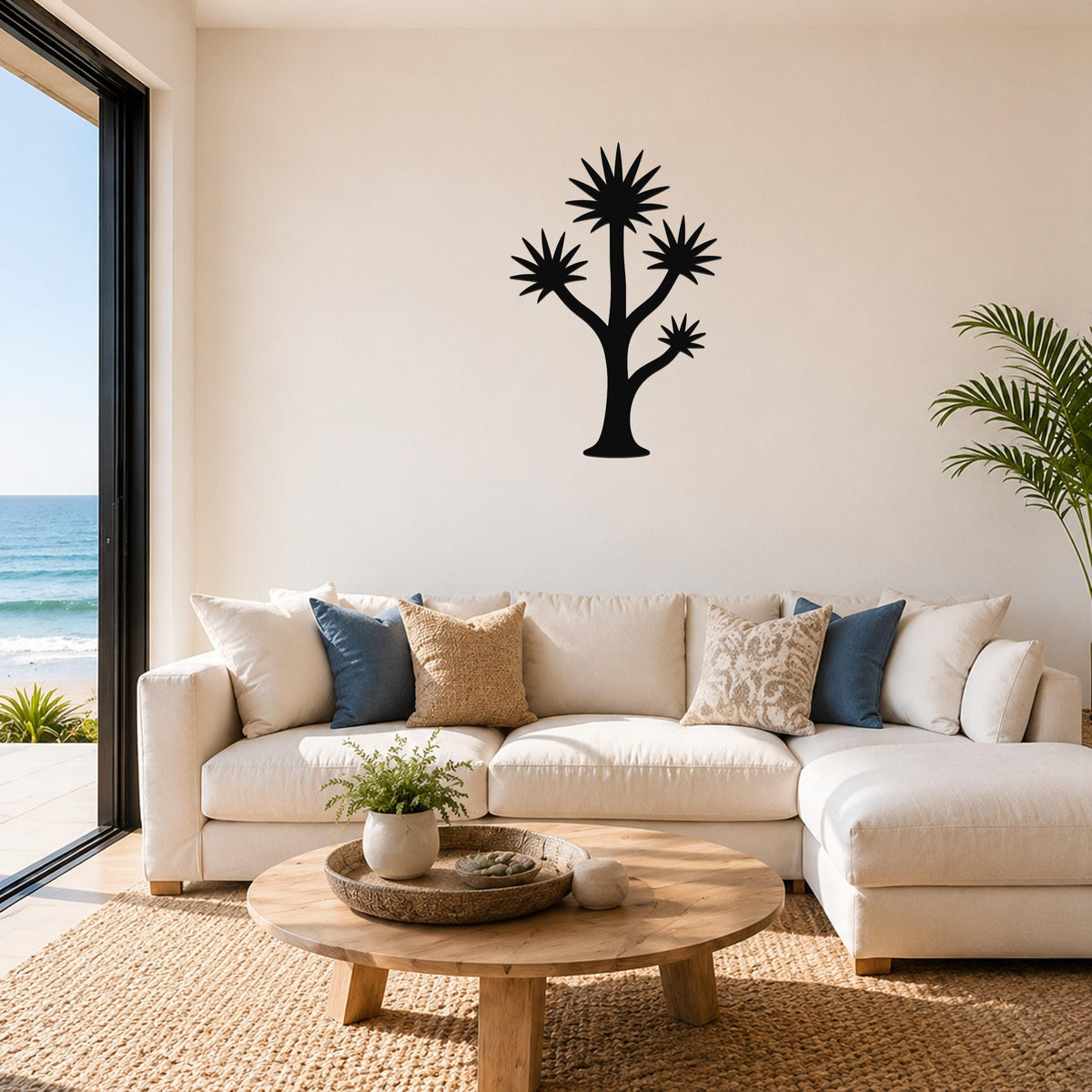 Black metal yucca tree wall art with starburst fronds and branching silhouette, mounted above a white sofa in a living room with ocean views.