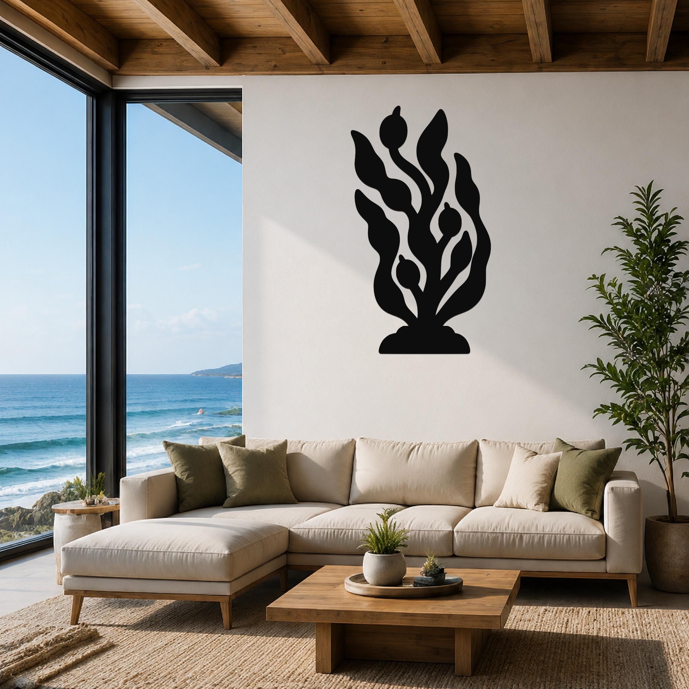 Black metal wall art in a kelp and seaweed silhouette design, mounted on a white wall above a beige sectional sofa in a living room with ocean views.