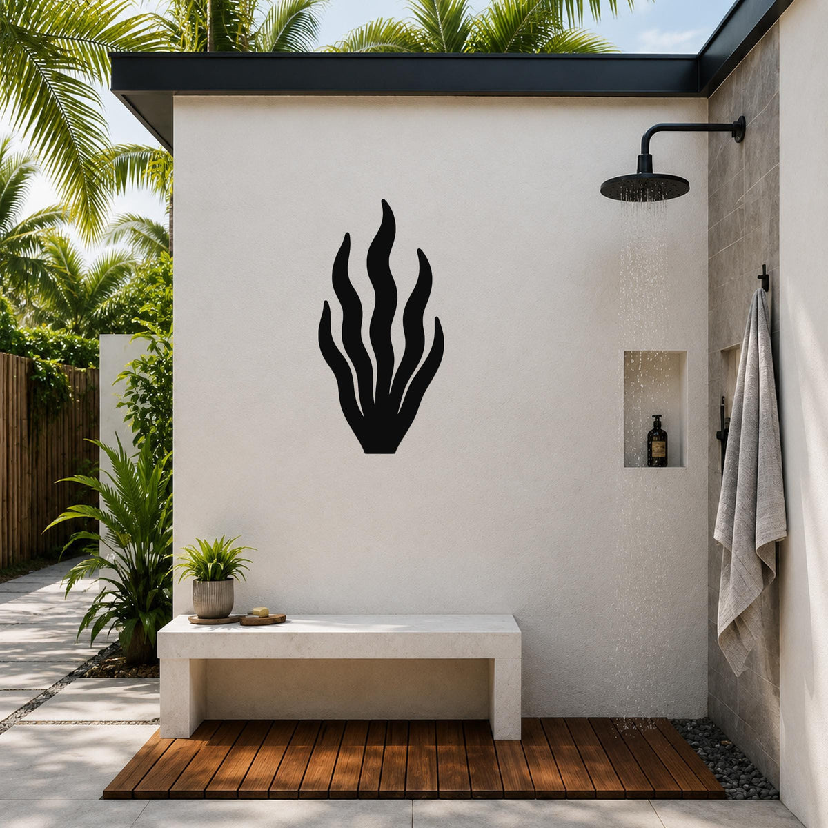 Black metal kelp wall art silhouette mounted on a white outdoor shower wall, above a stone bench in a tropical patio setting.