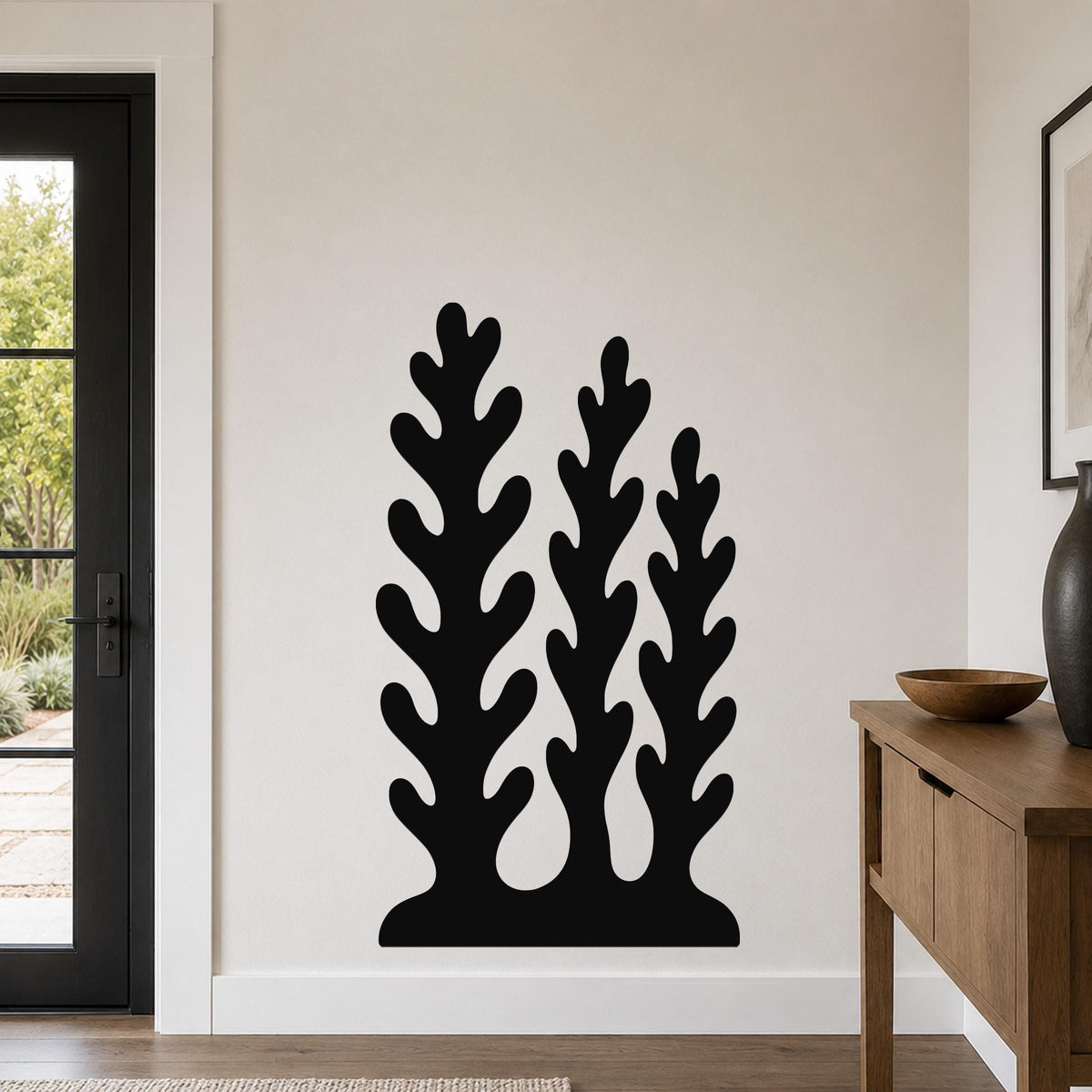Black metal wall art with a kelp and seaweed silhouette design, mounted on a light-colored wall in a modern entryway.