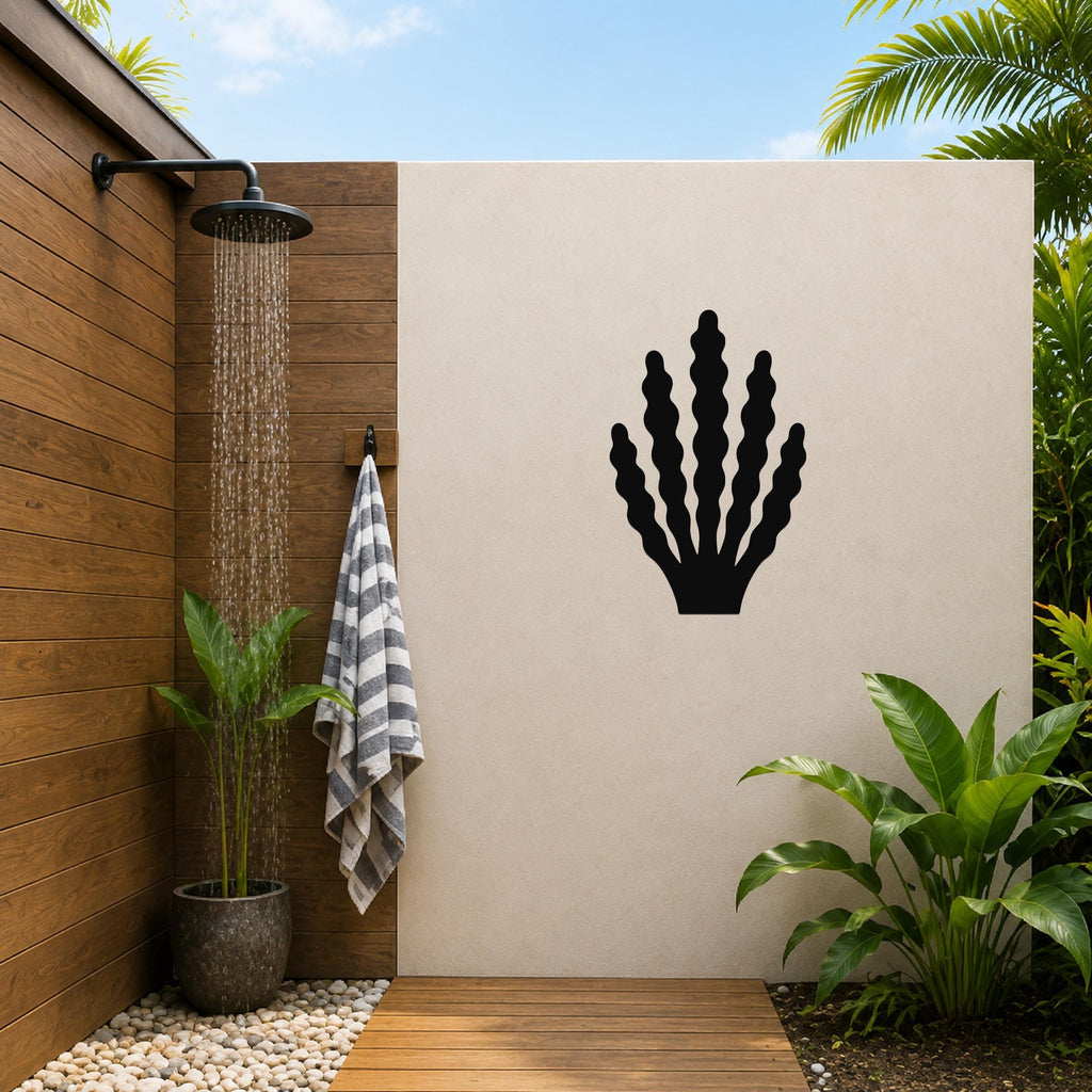 Black metal kelp wall art with wavy frond cutouts, mounted on a beige outdoor wall beside a wooden shower area.