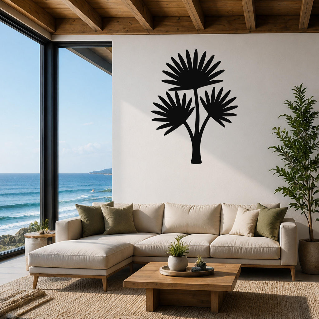 Black metal cutout palm tree wall art with three fan-shaped fronds, mounted on a white wall above a beige sectional sofa in a living room with ocean views.