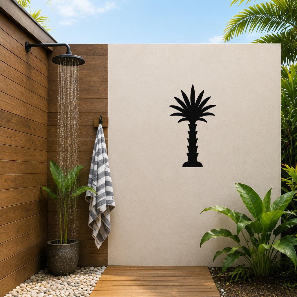 Black metal palm tree wall art silhouette mounted on a beige outdoor wall beside a wooden shower area with a running showerhead and tropical plants.