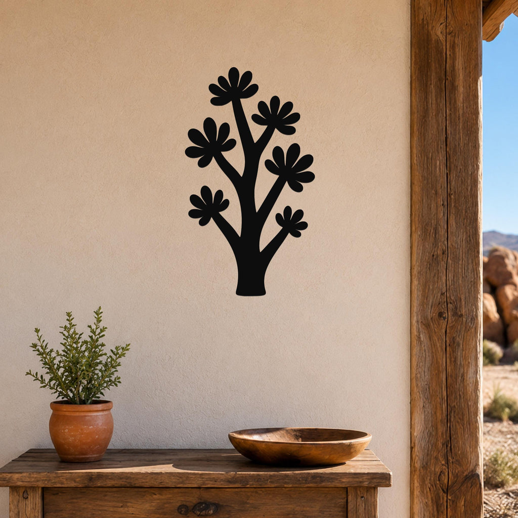 Black metal wall art in a stylized tree shape with flower cutouts, mounted on a beige wall above a wooden table in a patio setting.