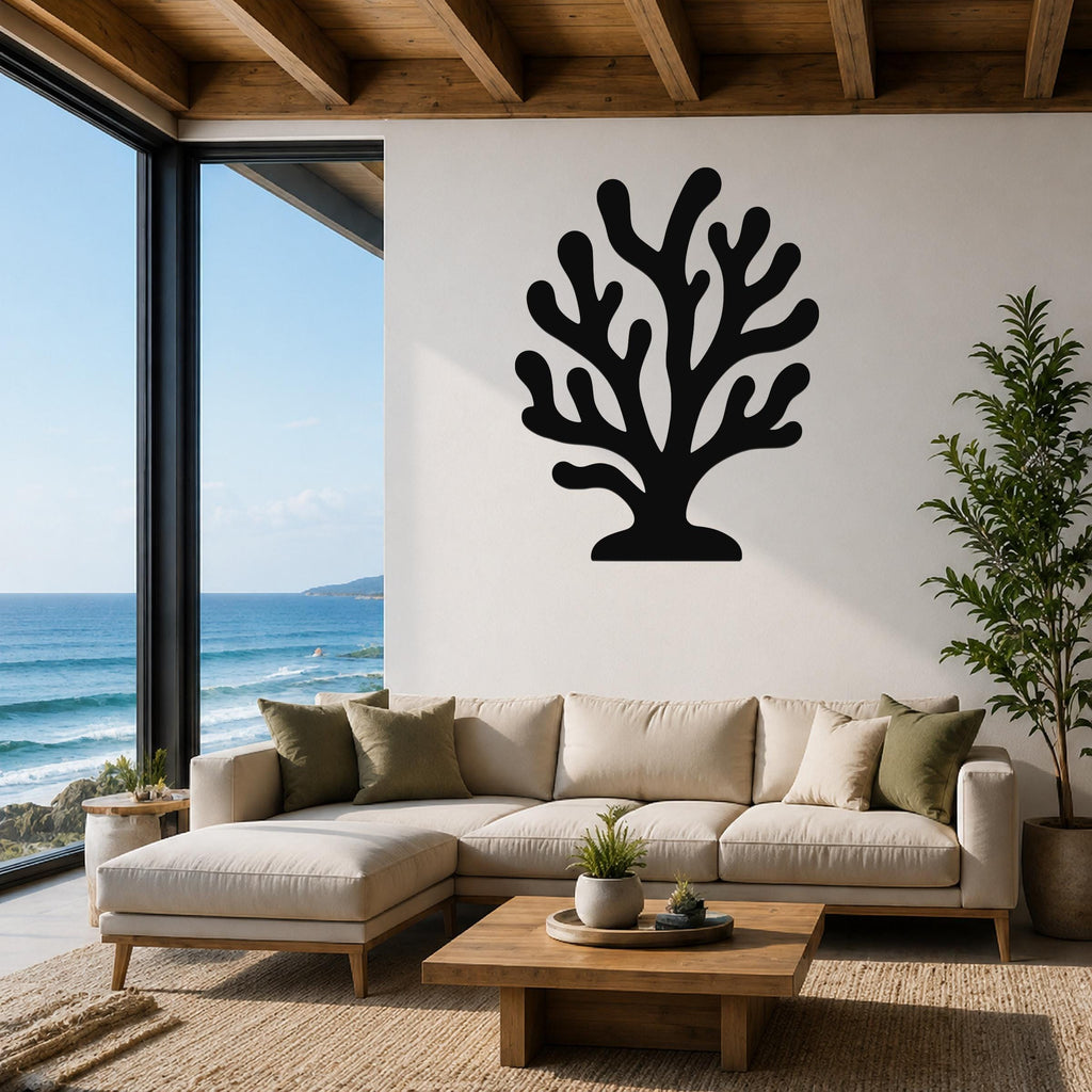 Black metal coral wall art with branching cutouts, mounted on a white wall above a beige sectional sofa in a living room with ocean views.