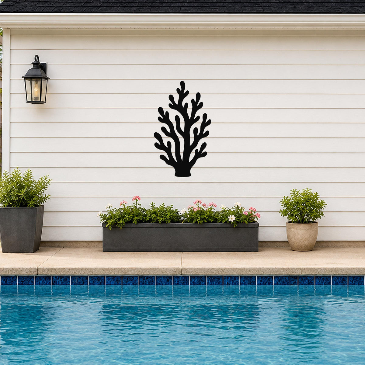 Black metal coral wall art with branching cutouts, mounted on a white horizontal siding wall above a poolside planter.