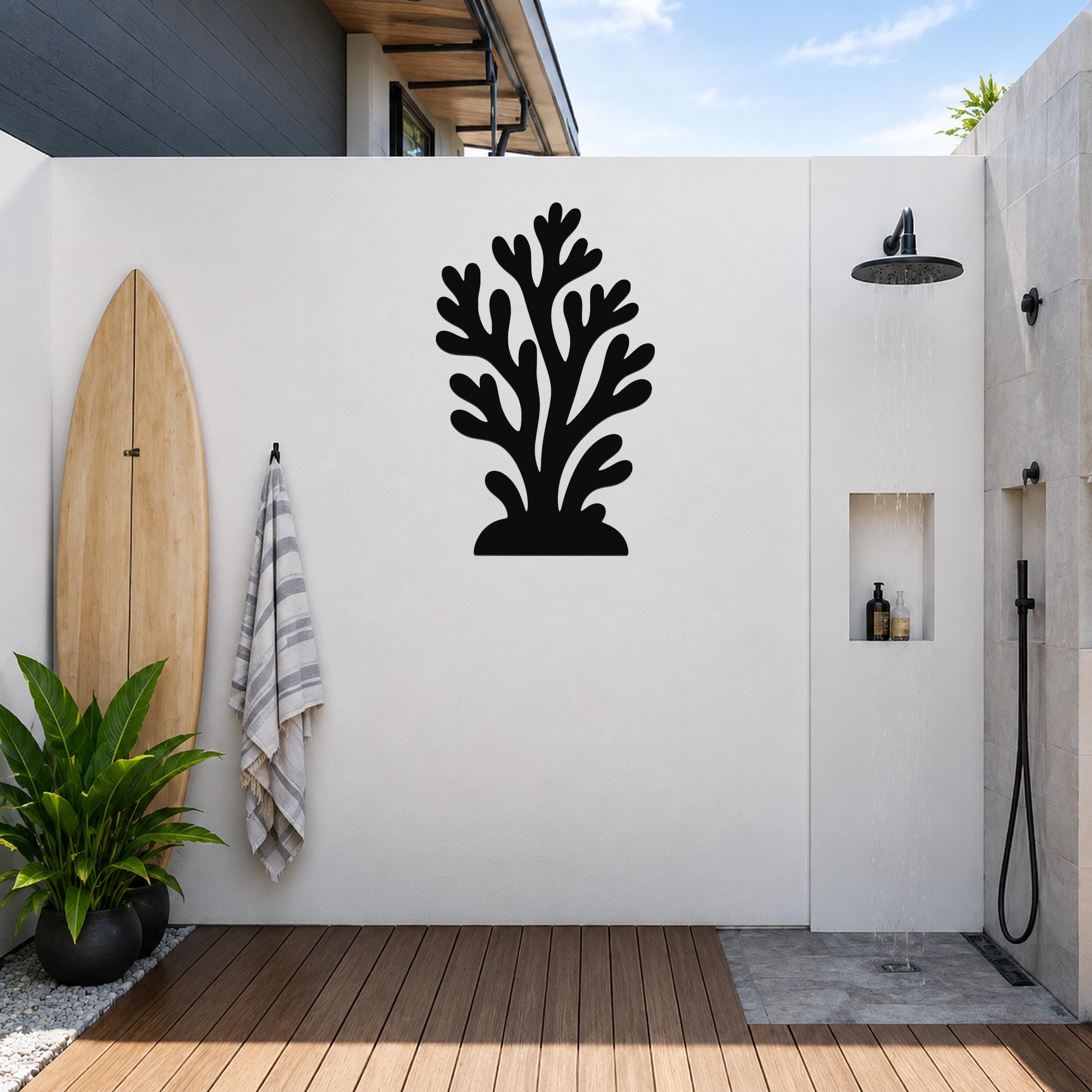 Black metal coral wall art with branching cutouts, mounted on a white outdoor wall above a wooden deck near a shower area.