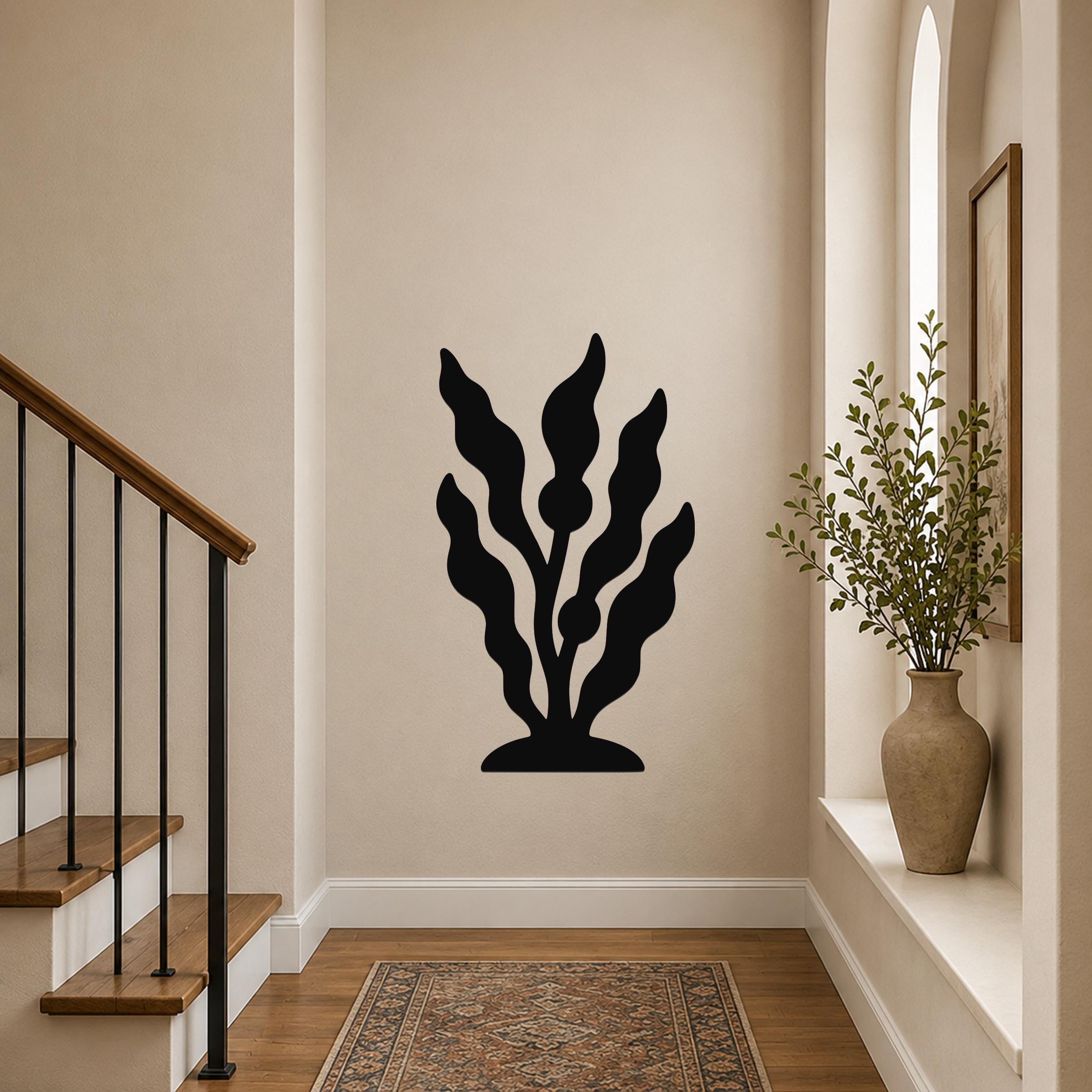 Black metal wall art in a kelp or seaweed silhouette design, mounted on a hallway wall above a patterned rug near a staircase.