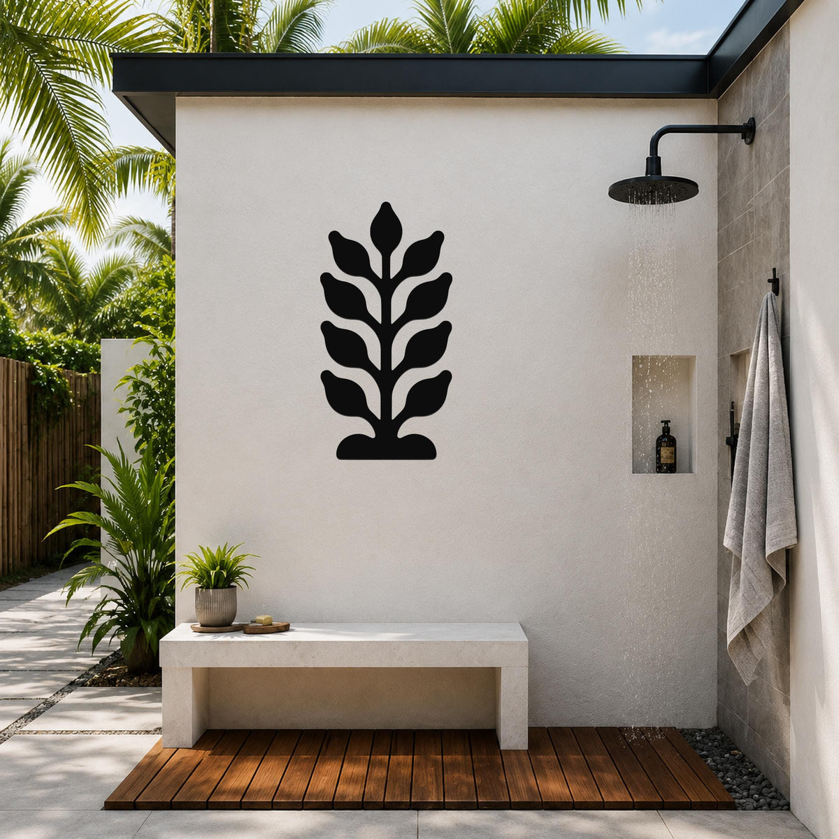 Black metal wall art with a leafy plant silhouette, mounted on a white outdoor shower wall above a concrete bench.