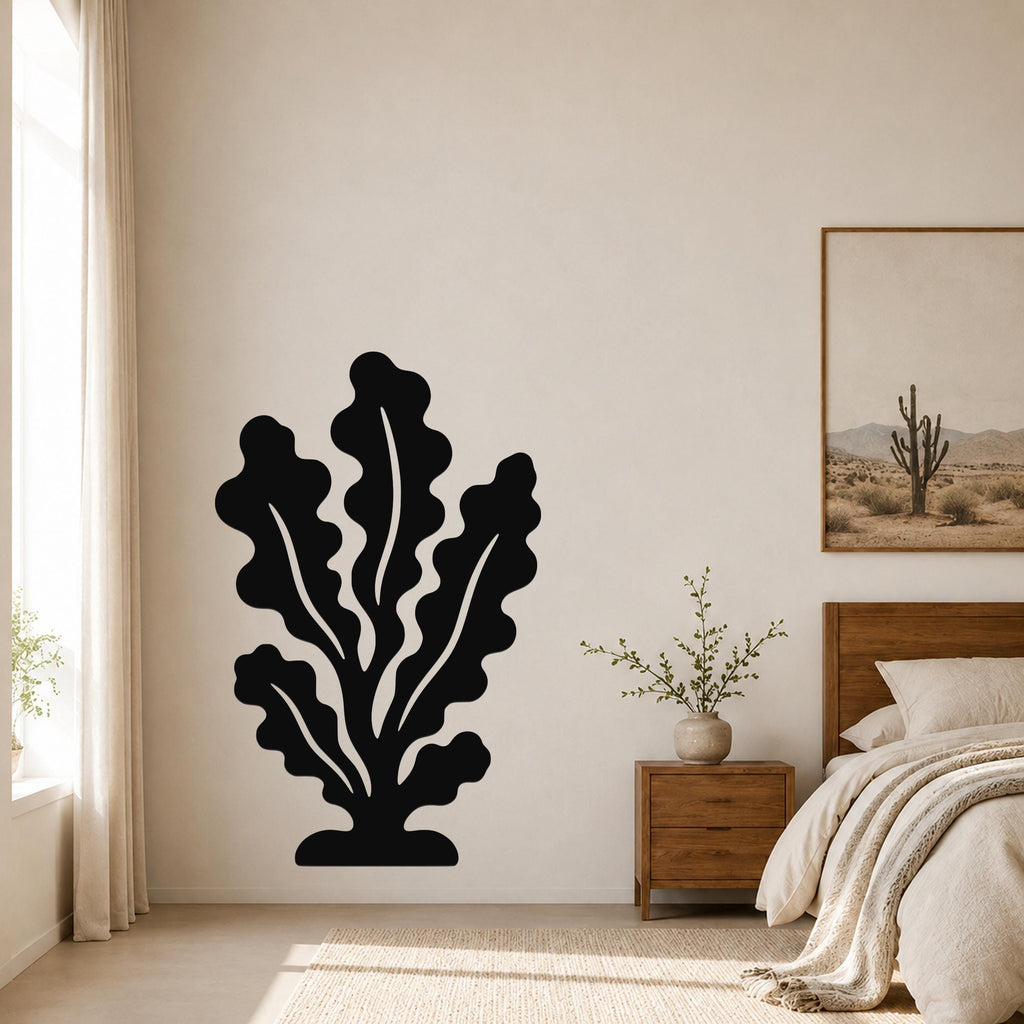 Black metal kelp wall art with leafy cutout design, mounted on a bedroom wall above a wooden nightstand.
