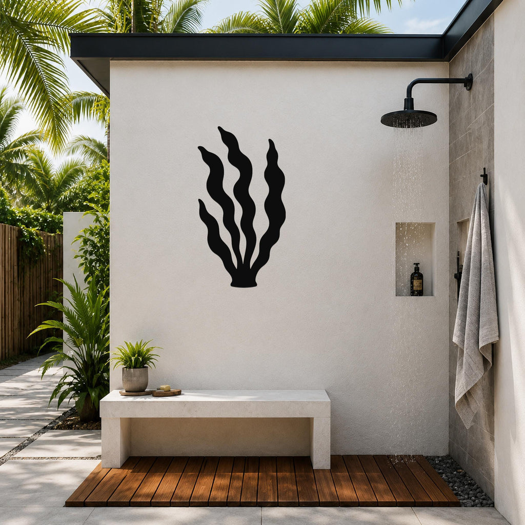 Black metal kelp wall art silhouette mounted on a white outdoor shower wall, above a concrete bench in a tropical patio setting.