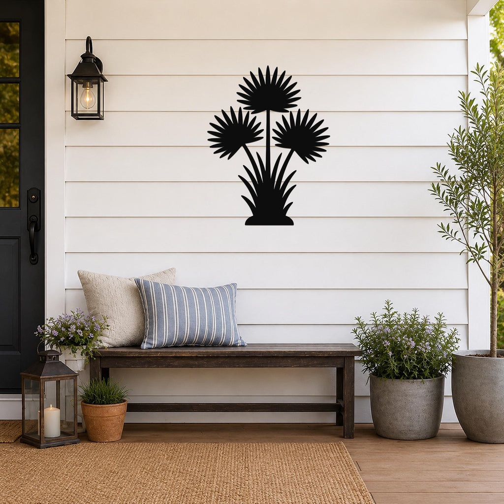 Black metal wall art in a fan palm tree silhouette with three fronds and a base, mounted on a white shiplap wall above a wooden bench on a porch.