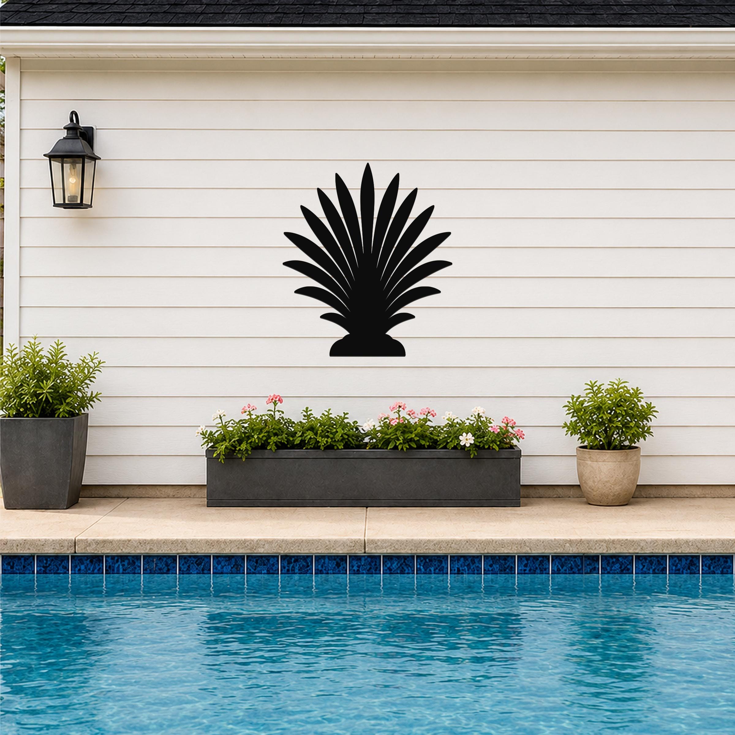 Black metal palm tree wall art silhouette mounted on a white horizontal siding wall above a poolside planter.