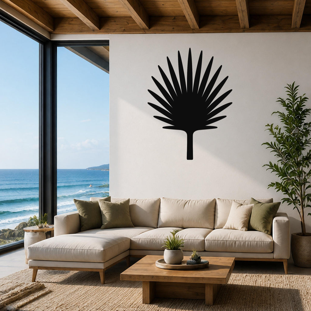 Black metal fan palm tree wall art silhouette mounted above a beige sectional sofa in a living room with ocean views.